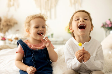 Cute toddler children, boy and girl, eating lolly pop at home