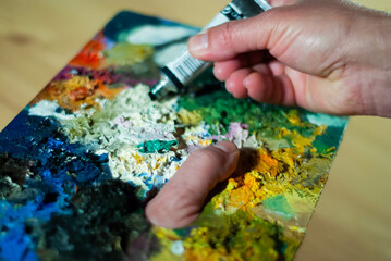Naklejka na ściany i meble Painter's hands taking a paint brush from his palette to paint an oil painting