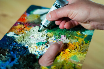 Naklejka na ściany i meble Painter's hands taking a paint brush from his palette to paint an oil painting