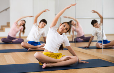 Fototapeta na wymiar Girl doing exercises in lotus pose with her family in gym.
