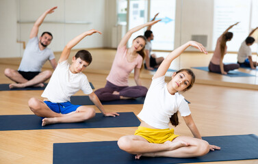 Fototapeta na wymiar Fit woman, man and teenage girl and boy performing yoga exercises on gymnastic mats at yoga studio, physical, emotional and spiritual family health concept