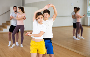 Cute preteen girl and boy siblings enjoying slow foxtrot in pair in dance studio during family...