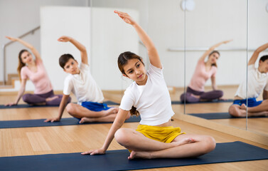 Fototapeta na wymiar Young girl exercising lotus pose with her family during group yoga training.
