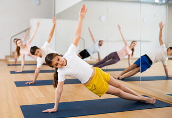 Plakat Positive pre-teen girl performing yoga exercises with brother and parents at gym, family health concept