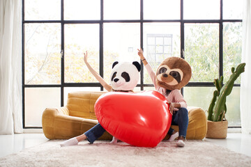 Funny women wearing animal mask bear panda holding big heart at home - Happy positive emotions...