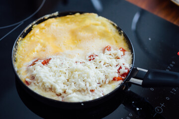 Frying pan on stove with omelet, melted cheese and tomatoes. breakfast