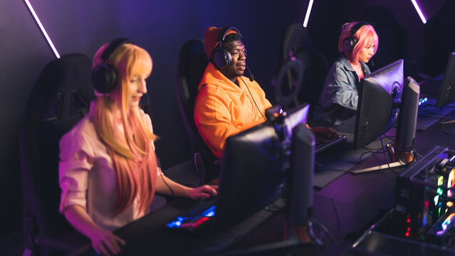 Online gaming team. Three interracial people sitting in an Internet cafe, playing on desktop computers, using professional headset. High quality photo