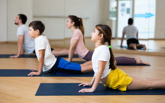 Sporty teen girl practicing yoga positions during family workout at fitness center, performing stretching asana Urdhva Mukha Shvanasana known as Upward Facing Dog
