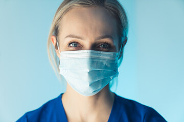 attractive young blonde European nurse smiling under the mask closeup studio shot blue background medical concept. High quality photo