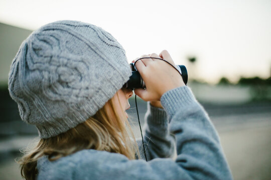 Female blond girl wearing beanie looking through binoculars