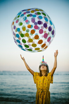 Young girl with blond hair throws a rainbow ball in front of ocean