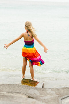 Blond caucasian girl in rainbow dress with wind on ocean