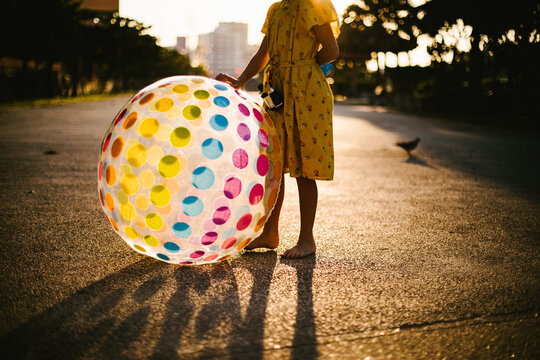 Girl stands in golden light with rainbow ball in yellow dress