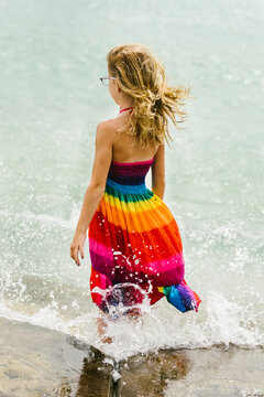 Blond girl stands in ocean while wind blows hair and waves hit legs