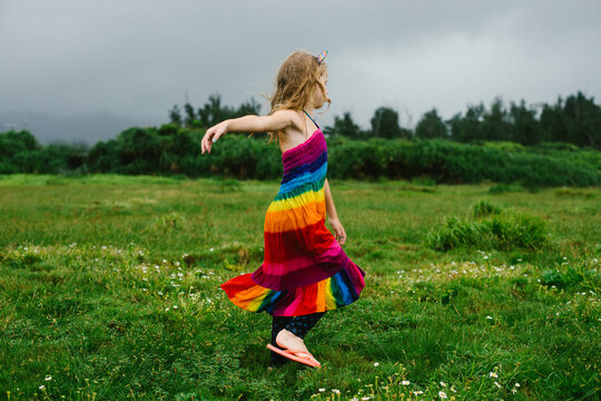 Young blond girl twirls in green grassy plain in rainbow dress
