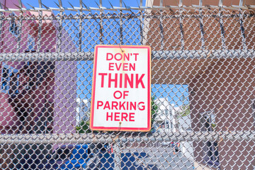 Don't even think of parking here signage on a metal mesh fence in San Francisco, California