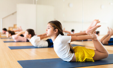 Concentrated teen girl doing back bending asana Dhanurasana known as Bow Pose during yoga workout...