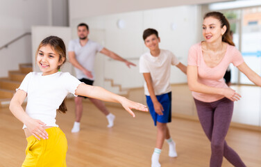 Happy sporty family of four enjoying active dance in modern studio. Focus on smiling brunette...