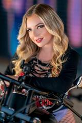 Fototapeta na wymiar A Lovely Blonde Model Poses Outdoors With Her Motorcycle In A Large City Environment