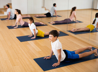 Fototapeta na wymiar Family of four practicing yoga on mats at gym, concept of families exercising together