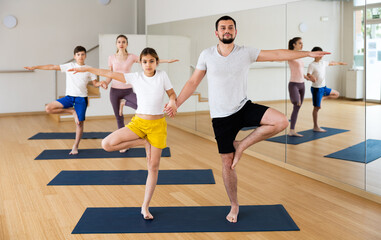 Naklejka na ściany i meble Teen girl and boy exercising with mother and father at couple yoga class, family practicing self-care