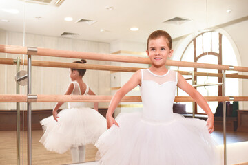 A cute little ballerina in a dance hall with large mirrors.she is ready to dance.