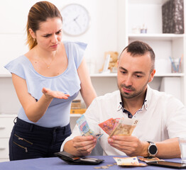 Man is counting money with wife at the table at home.