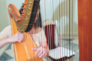 Female musician harpist playing wooden harp  during symphonic concert on a stage, with other musicians in the background, close up hands of the woman playing decachord