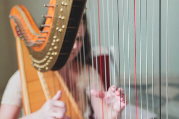 Female musician harpist playing wooden harp  during symphonic concert on a stage, with other musicians in the background, close up hands of the woman playing decachord