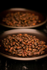 Pine nuts on a plate on a black background. Healthy food and snacks.Unpeeled pine nuts close-up in a ceramic bowl on a black marble background. dark key 