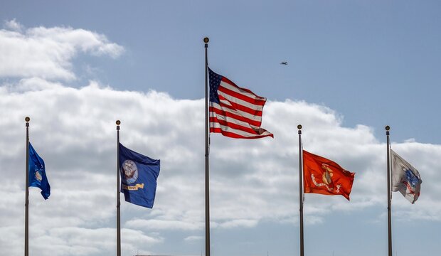 American flag and military flags waving in the wind with a small plane in the sky on a spring afternoon in Ocala, Florida.