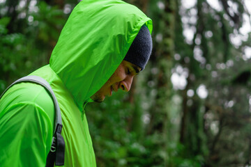 smiling young latino man on a jungle hike in a fluorescent waterproof jacket.