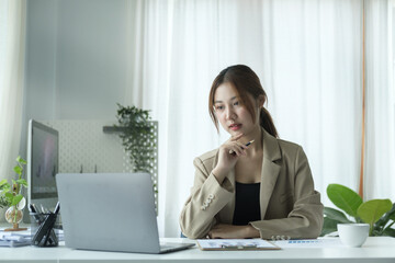 Thoughtful young businesswoman sitting at her workplace and reading information on laptop computer.