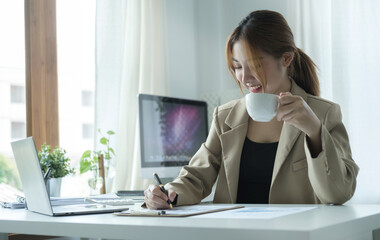 Attractive young businesswoman drinking coffee and working at modern office.