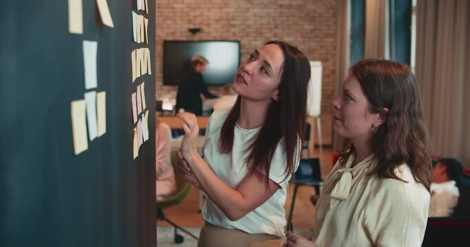 Two happy young beautiful female European business managers, partners work together with stickers at office slow motion.