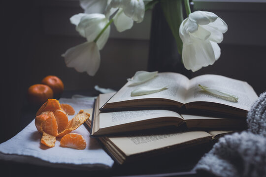 Tabletop arrangement of white flowers three open books and tangerines on a rainy day.