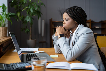 Young sad african-american businesswoman looking thoughtfully at open laptop, upset black female...
