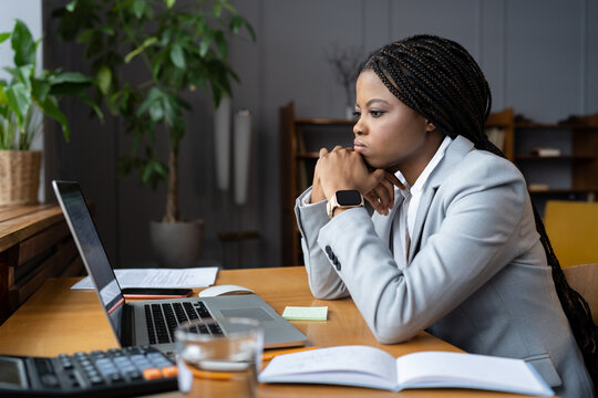 Young sad african-american businesswoman looking thoughtfully at open laptop, upset black female employee trying to focus on work, failing to complete task on time or having no motivation to work