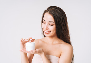 Beauty portrait of happy smiling asian woman with dark long hair put day nourishing moisturizer cream on clean fresh skin face and hands on white background
