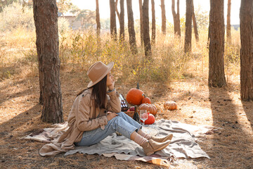 Young woman having romantic picnic in forest on autumn day
