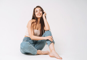 Portrait of happy young beautiful asian woman with dark long hair in jeans sitting on white background isolated
