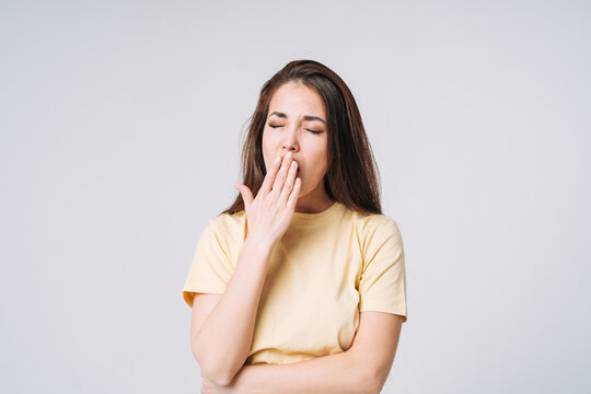 Young yawning asian woman winner with long hair in yellow shirt on grey background