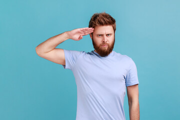 Portrait of responsible patriotic bearded man saluting with respect as if soldier waiting order...