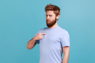 This is me. Portrait of self-confident narcissistic bearded man standing pointing himself, feeling self-important, proud, famous. Indoor studio shot isolated on blue background. - obrazy, fototapety, plakaty