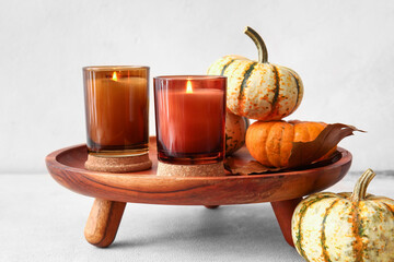 Wooden stand with burning candles and pumpkins on light background, closeup
