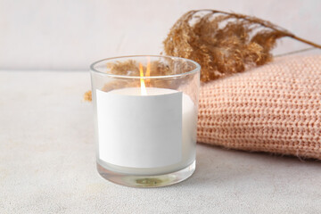 Glass holder with burning candle, reed flowers and sweater on light background, closeup