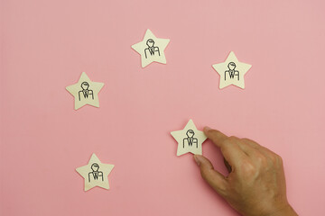 Top view of human resources and recruiting business or team leader management concepts. Hand adult Asian man holding difference of people icon on  wooden block. Objects on pink paper background.