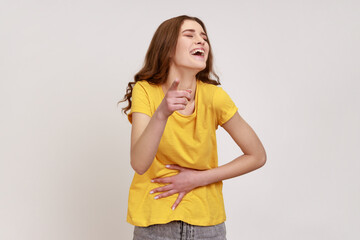 Hey, you are ridiculous! Teenager girl in yellow T-shirt laughing, holding stomach and pointing to...