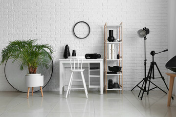 Workplace and different equipment near white brick wall in interior of modern photo studio