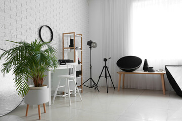 Interior of light photo studio with comfortable workplace and different equipment
